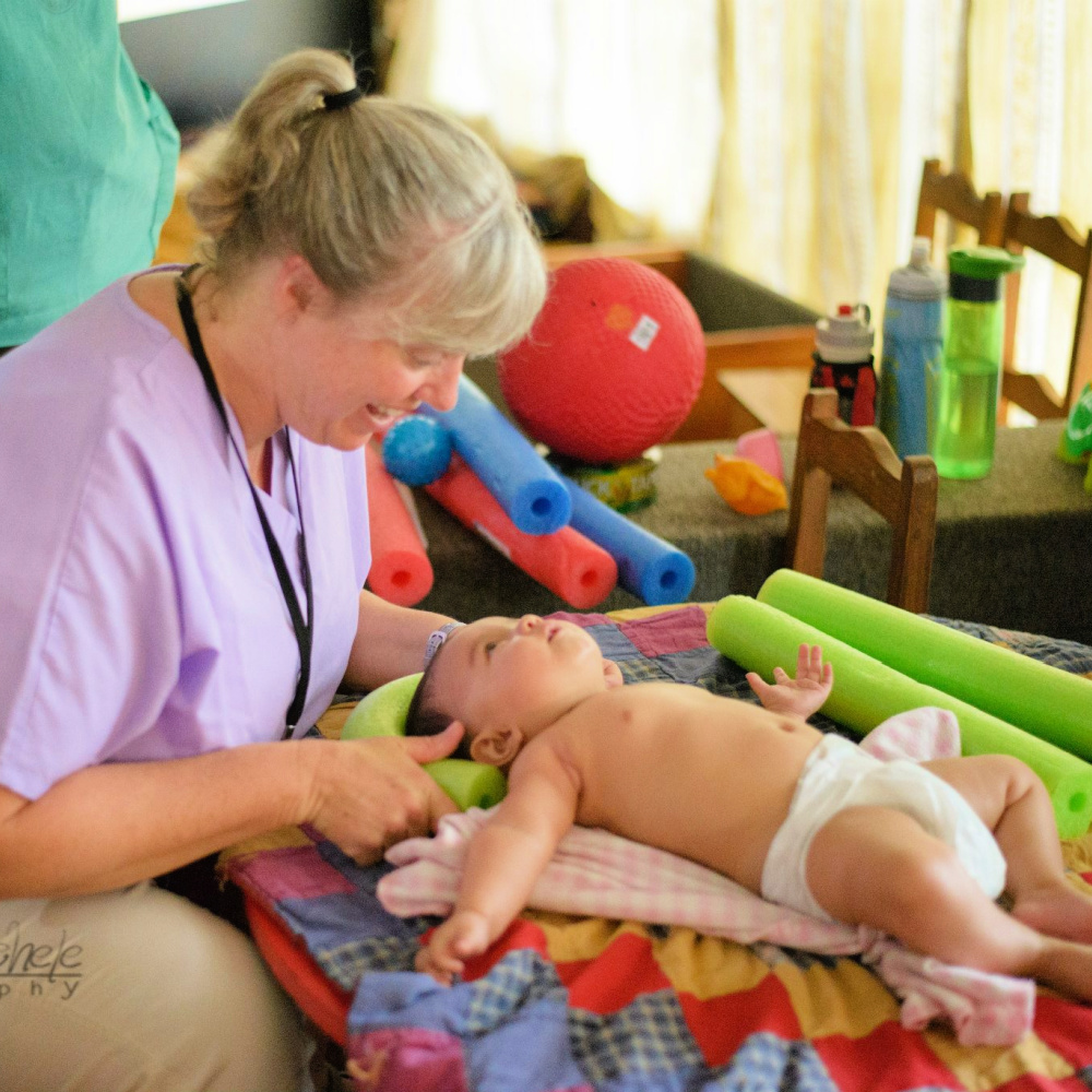 A BRIGHT Children International team member sits with a baby, who is laying on their back looking up at the team member.