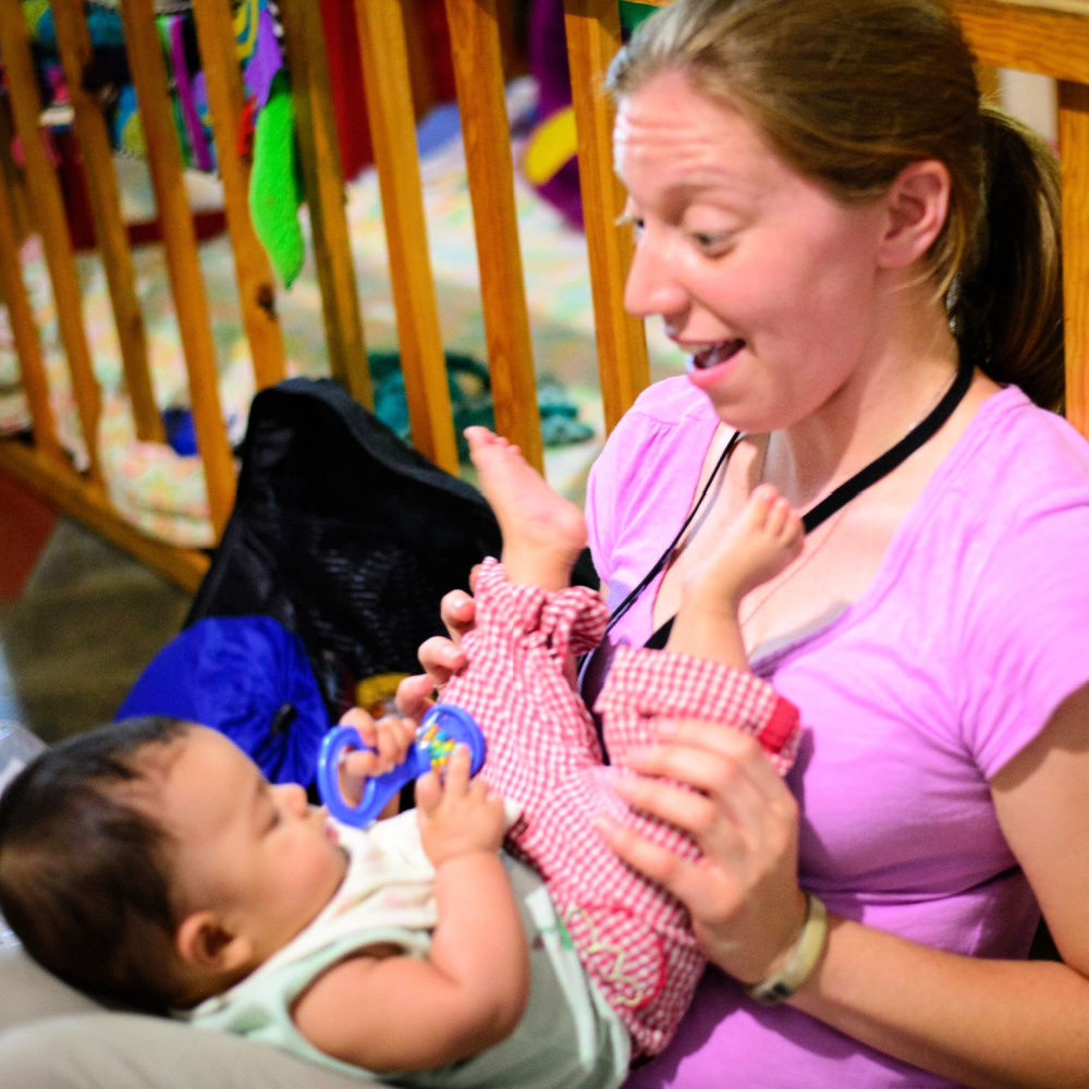 A therapist sitting with a baby on her legs, engaging the baby with toys and music.