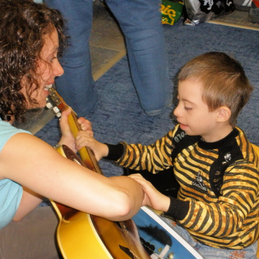 A young boy with Down syndrome, strumming the strings of a guitar along with the help of a BRIGHT Children International music therapist.