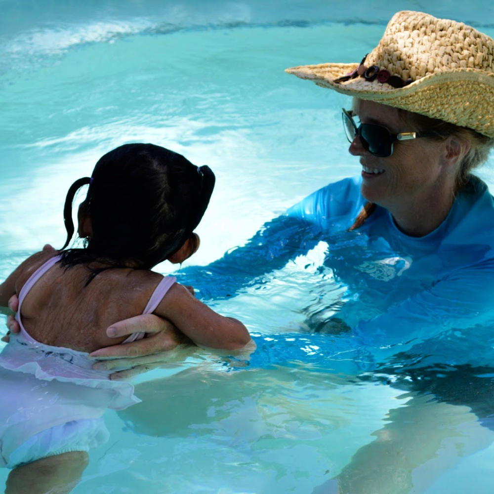 An aquatic therapist holds onto a young child as they move through a pool together.