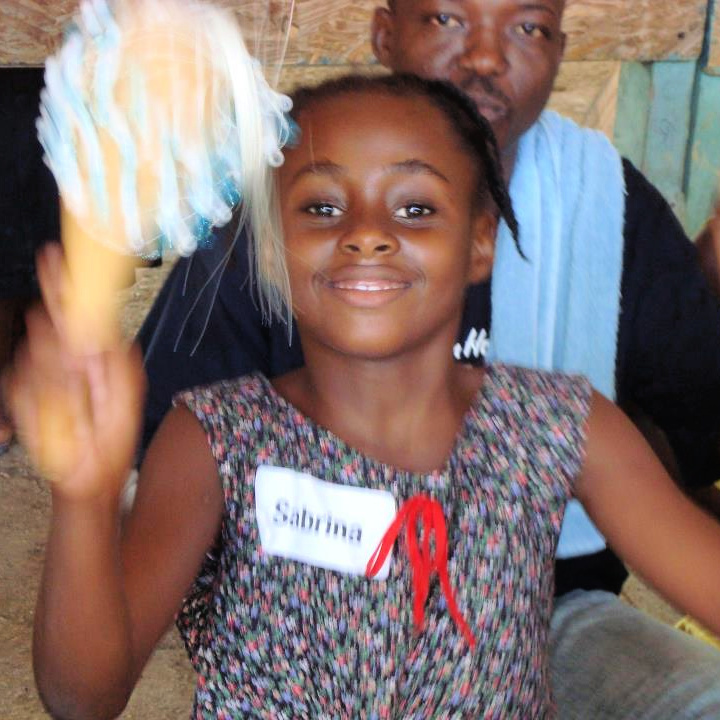 A young girl with dark skin shaking a shaker during a therapeutic music experience in Haiti in 2011.