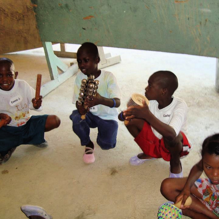 A group of children immersed in a therapeutic music experience in Haiti in 2011. They are playing claves, jingle bells, a cabasa, and a variety of shakers.