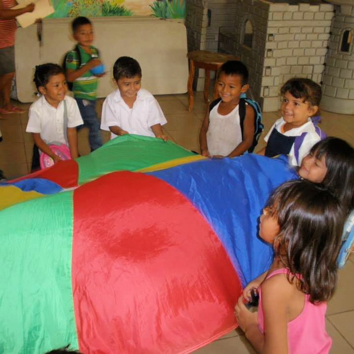 A group of young children all gathered around a colorful rainbow-colored parachute.