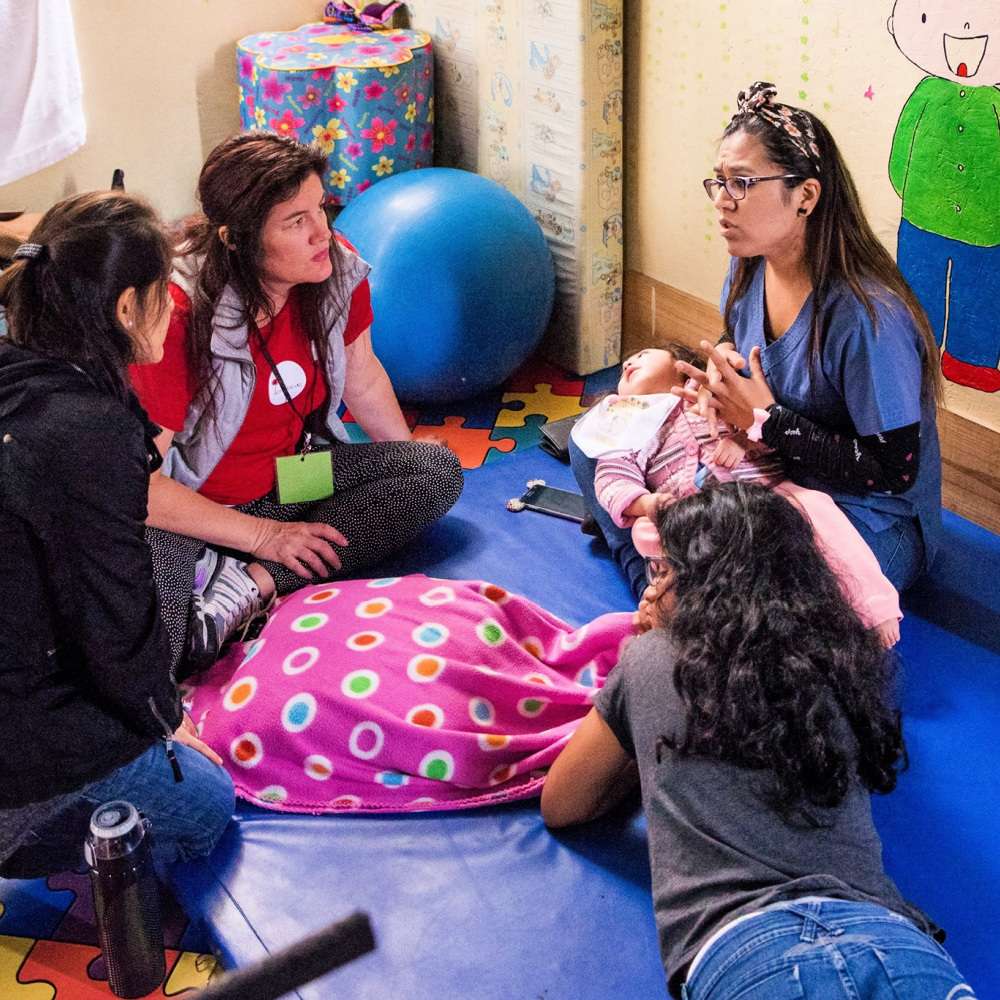 A group of adults sit in a circle on the floor, discussing therapeutic techniques and support for children with special needs.