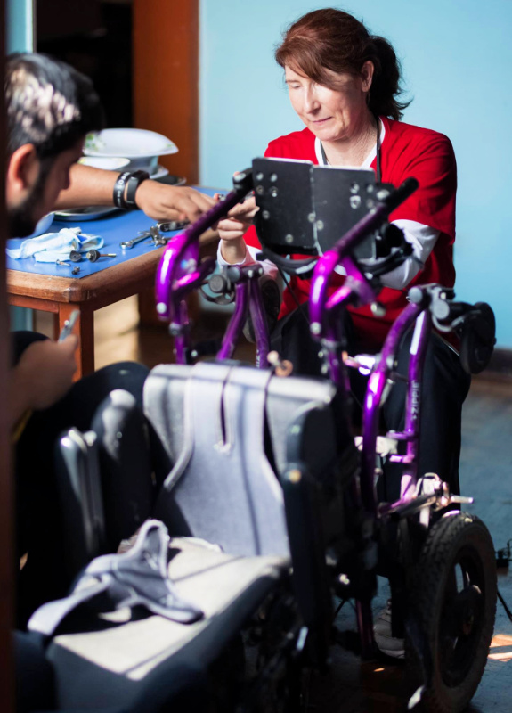 A team of two people work together to outfit and repair a wheelchair and standing device.
